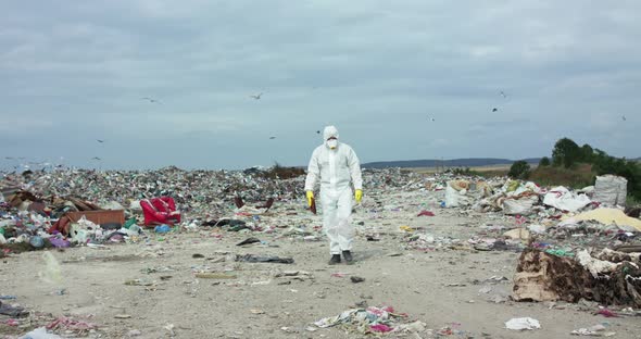 Ecologist in Protective Suit and Gas Mask Walking with Tablet Near Polluted Land