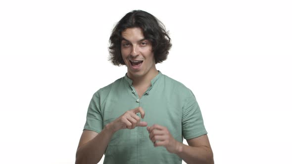 Handsome Hispanic Man in Green Shirt Pointing at Himself and Raising Eyebrows Cheeky Showing Heart
