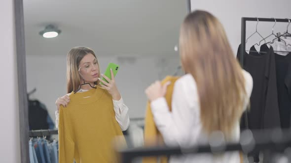 Millennial Shopper Reflecting in Mirror Taking Selfie with New Yellow Warm Sweater