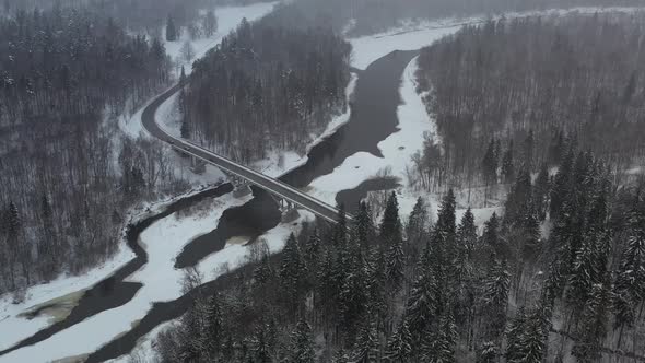 Forest valley Bridge over a frozen river in winter snowstorm