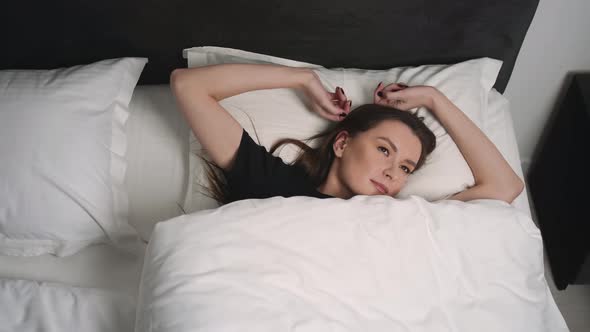 Portrait of Relaxed Smiling Woman Wakes Up on a White Pillow in Bed