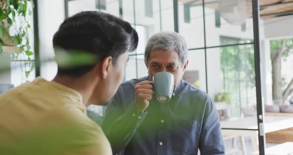 Man sipping coffee from mug while listening to son's conversation in kitchen at home