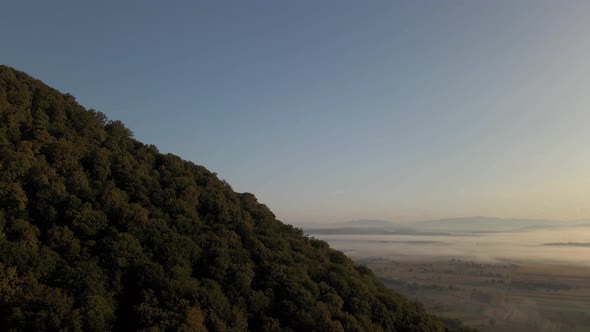 Slow flight around forest covered hill at edge of vast flat lands