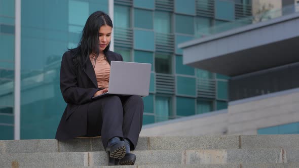 Young Businesswoman Freelancer Sitting Outdoors Working on Internet Typing on Laptop Using Computer
