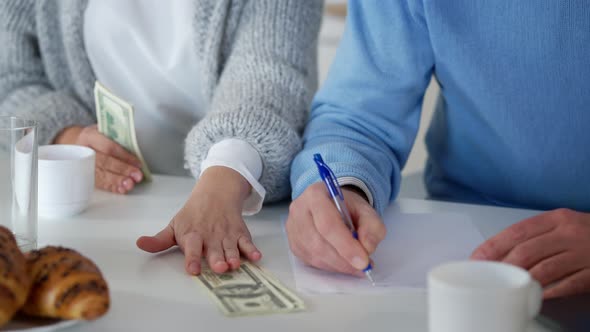 Female Hands Counting Cash Money As Male Writing Family Budget on Paper