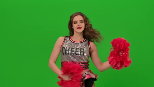 An Adorable Cheerleader in Uniform with Red Pompoms Performs a Jubilant Dance