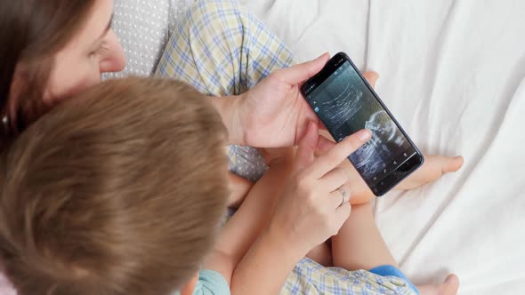 Closeup of Young Woman Showing Baby Ultrasound Image To Her Little Son on Smartphone