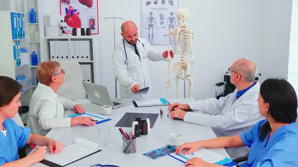 Doctor Explaining Radiography in Front of Medical Staff Using Skeleton