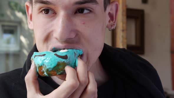 A Young Man Appetizingly Bites Off a Sweet Donut with Cream