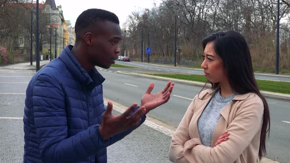 A Young Black Man and a Young Asian Woman Argue in a Street in an Urban Area