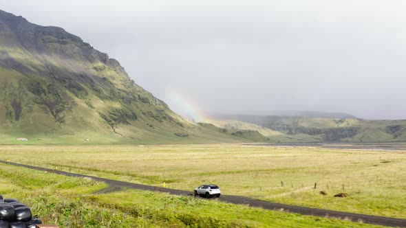Aerial of a Car Driving on a Mud Dirt Road Between Green Fields in Iceland