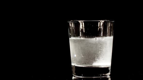 Pill Aspirin Falling Down in Glass with Water on Black Background