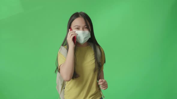 Asian Girl Student Wearing A Mask And Talking On Mobile Phone While Running On Green Screen