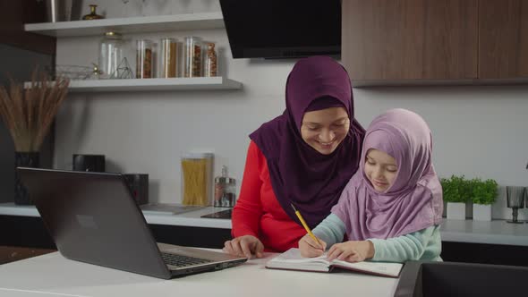 Positive Charming Arab Hijab Mother and Lovely Preschool Daughter Studying Together Indoors