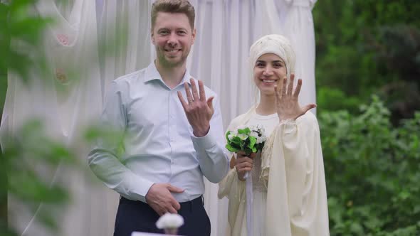 Loving Happy Middle Eastern Bride and Caucasian Groom Showing Wedding Rings Looking at Camera