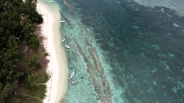 Slow aerial shot of exotic island with golden beach and boats swimming on clear water