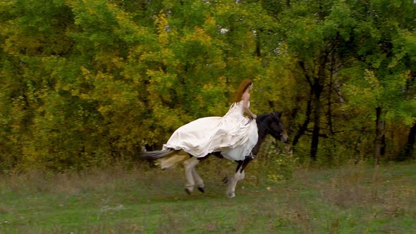 Red-haired Fiancee in Wedding Dress Riding Galloping Horse Near Wood