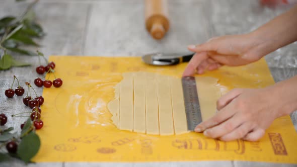 Close-up of person cutting dough into strips while preparing traditional cherry pie