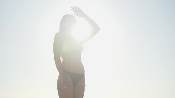 Side View of Beautiful Young Woman in Swimsuit and Face Mask Standing in Sunrays and Looking at