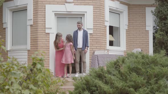 Happy Family Standing on the Porch Together. Mother and Father Kissing Goodbye To Little Daughter