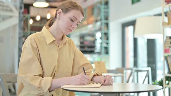 Focused Young Woman Doing Paperwork in Cafe