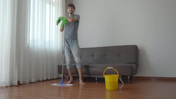 A Young Man in Green Rubber Gloves Washes Floor in an Apartment. Cleaning Service Concept. Gender