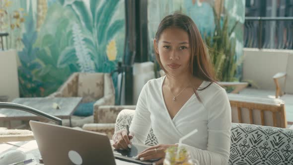 A Young Asian Girl Works at Her Laptop in a Rooftop Cafe in the City