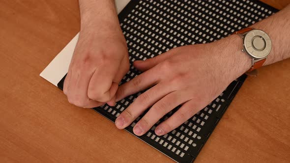 A Man Uses a Special Stencil and Stylus to Write a Letter in Braille