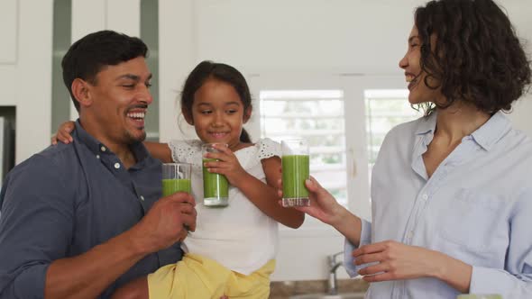 Happy hispanic family with daughter having green smoothie