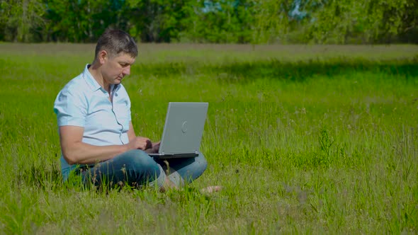 Businessman Works Behind a Laptop Sitting on the Grass