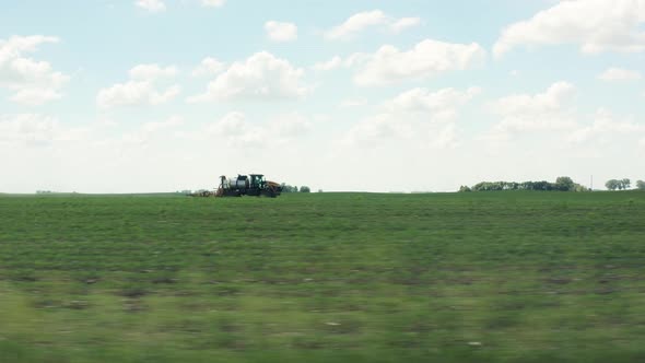 Aerial side view, tractor driving fast spraying pesticide on farm crops