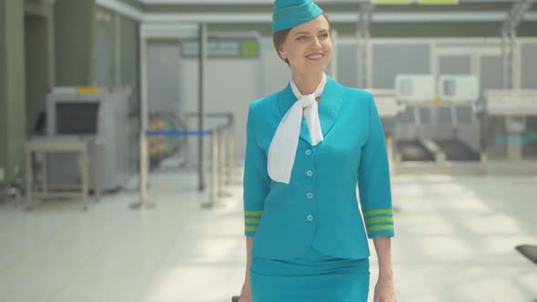 Gorgeous Smiling Stewardess Walking with Travel Bag in Airport. Portrait of Confident Positive