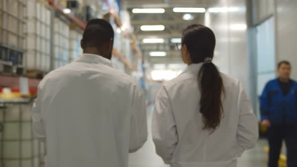 Back View of African and Caucasian Engineers in Lab Coats Examining Industrial Warehouse