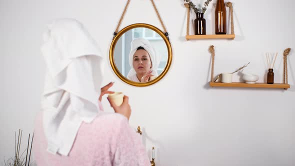 Woman Applying Creme on Face in Front of Mirror