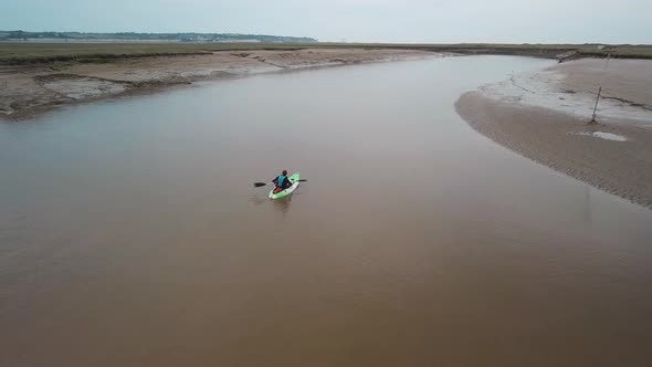 Man kayaking on meandering river, drone pans round kayaker.