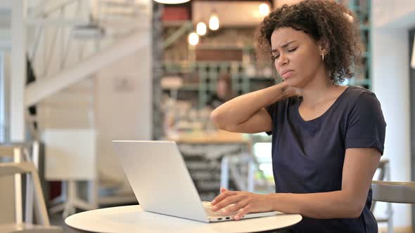 Young African Woman with Neck Pain Using Laptop in Cafe 