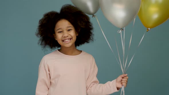 Cheerful little girl at her birthday party. Female child holding a lot of balloons