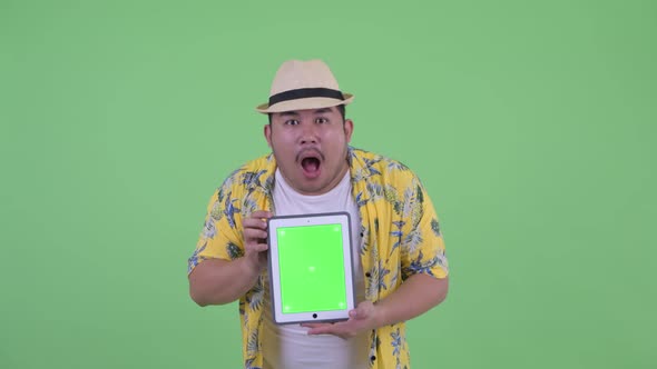 Happy Young Overweight Asian Tourist Man Showing Digital Tablet and Looking Surprised