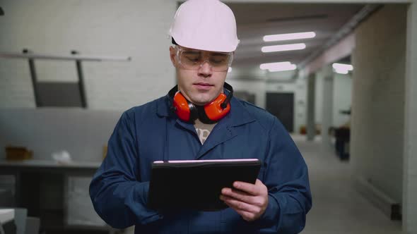 A Male Factory Worker Uses a Tablet in the Workshop
