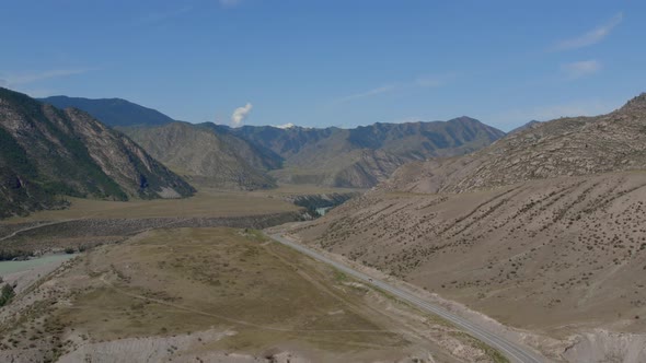 Traffic cars on road between mountains of Altai under clear blue sky