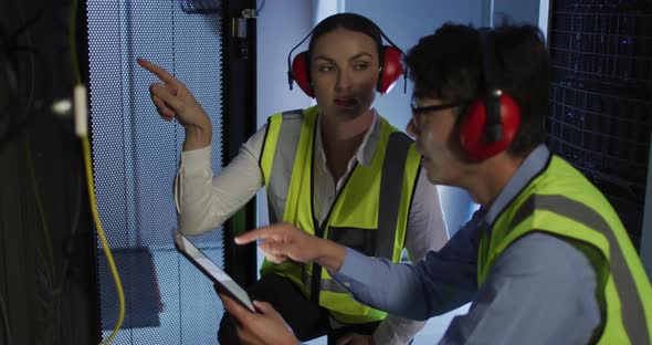 Diverse female and male it technicians wearing headphones using tablet checking computer server