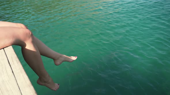 Woman Playing With Legs At Sea. Girl Playing With Feet In Ocean Off Edge Of Pier.