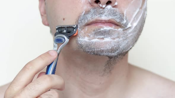 young man with shaving foam on face is smiling.guy using razor to shave beard.feeling pain.daily 