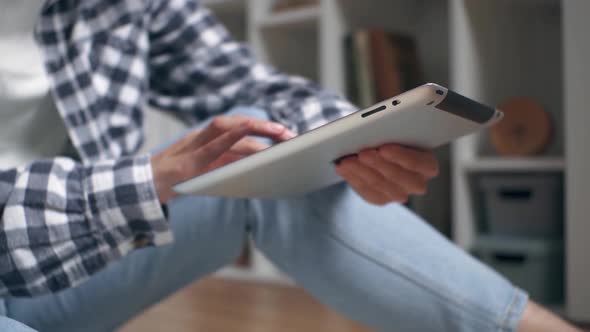 Hands Are Holding A Tablet. The Girl Sits On The Floor And Holds A Tablet Holding It In Her Hands