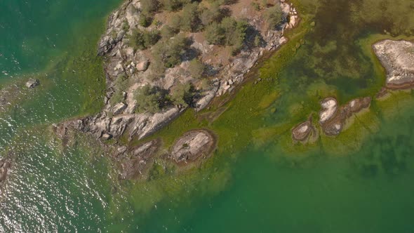 Drone flying up and away from a small island with green see thru water sea