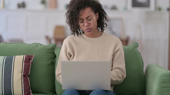 Young African Woman with Laptop Thinking on Sofa 