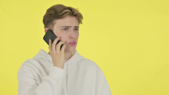 Young Man Talking Angry on Phone on Yellow Background