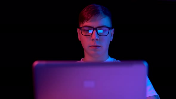 Young Man with a Laptop. A Man Uses a Laptop. Blue and Red Light Falls on a Man on a Black