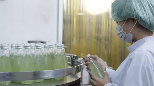 Asian Female supervisor inspecting bottle of herb drink production line