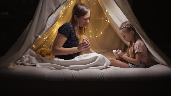 A Happy Mother Does a Foot Massage Her Daughter in a Tent in the Living Room